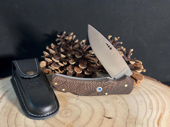 A pocket knife with a hand-finished Paduk wood handle and leather sheath — genuinely beautiful everyday carry craft that looks like it belongs in a wood shop portfolio.