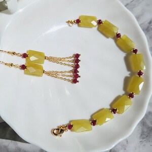 May include: A set of gold earrings and a bracelet featuring yellow and red gemstone beads. The earrings have a dangling chain with red beads. The bracelet has a clasp closure.