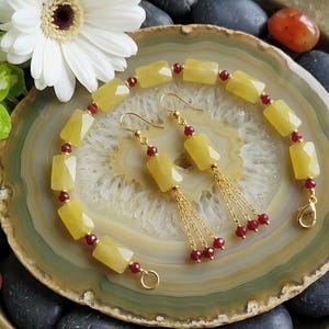 May include: A jewelry set featuring a bracelet and earrings. The bracelet and earrings have yellow rectangular beads with red accents. The earrings have gold chains and red beads. The set is displayed on a decorative plate.