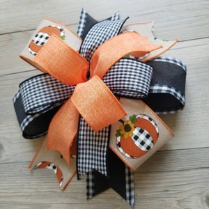 Op de afbeelding: Een herfstthema strik met zwart-wit geblokt lint, oranje lint en een jute lint met een pompoenontwerp.