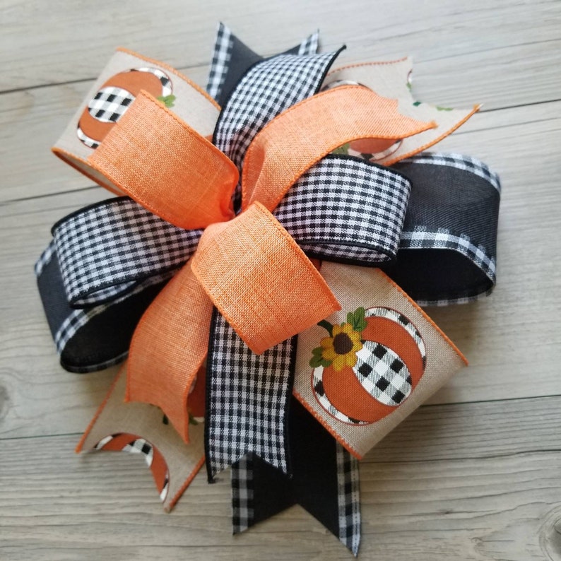 Op de afbeelding: Een herfstthema strik met zwart-wit geblokt lint, oranje lint en een jute lint met een pompoenontwerp.