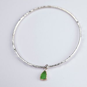 May include: A silver bangle bracelet with a hammered finish and a green glass charm.
