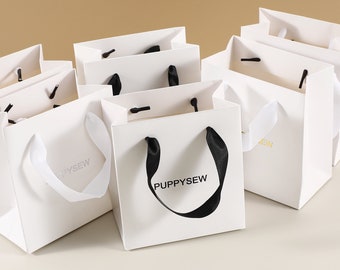 May include: Multiple white paper gift bags with black handles. Some bags have the text "PUPPYSEW" printed on them in black.