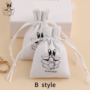 May include: Two white cotton drawstring bags with a black and white illustration of a dog sitting in a box. The bags have the text "PUPPYSEW" printed on them. The bags are labeled "B style".