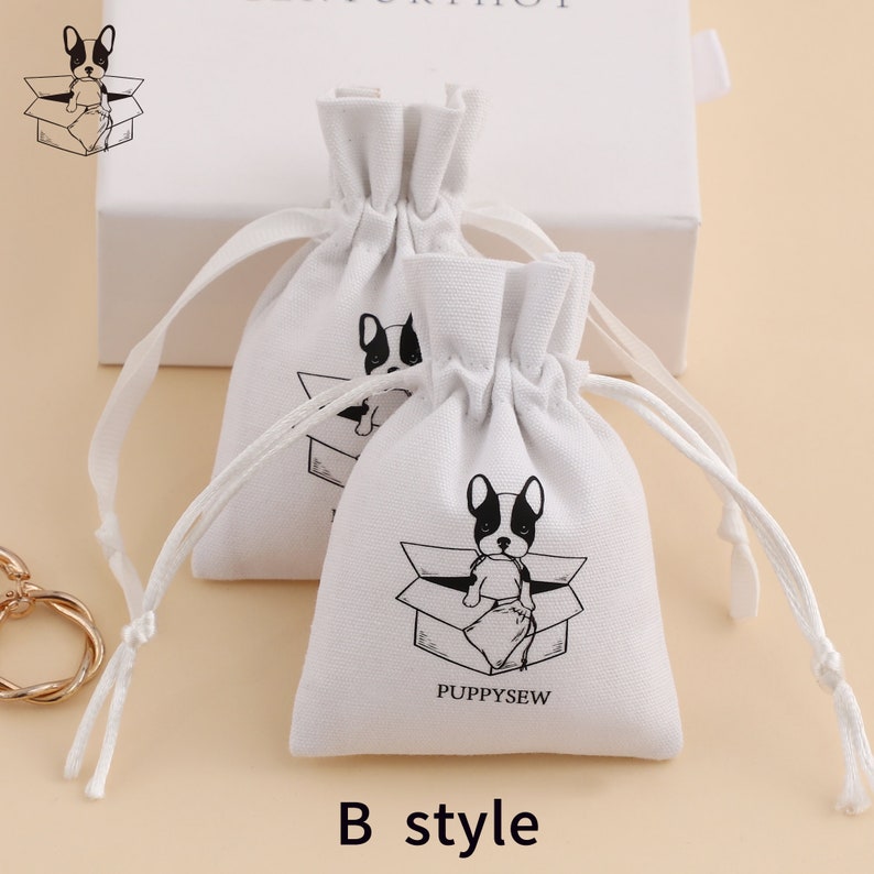 May include: Two white cotton drawstring bags with a black and white illustration of a dog sitting in a box. The bags have the text "PUPPYSEW" printed on them. The bags are labeled "B style".