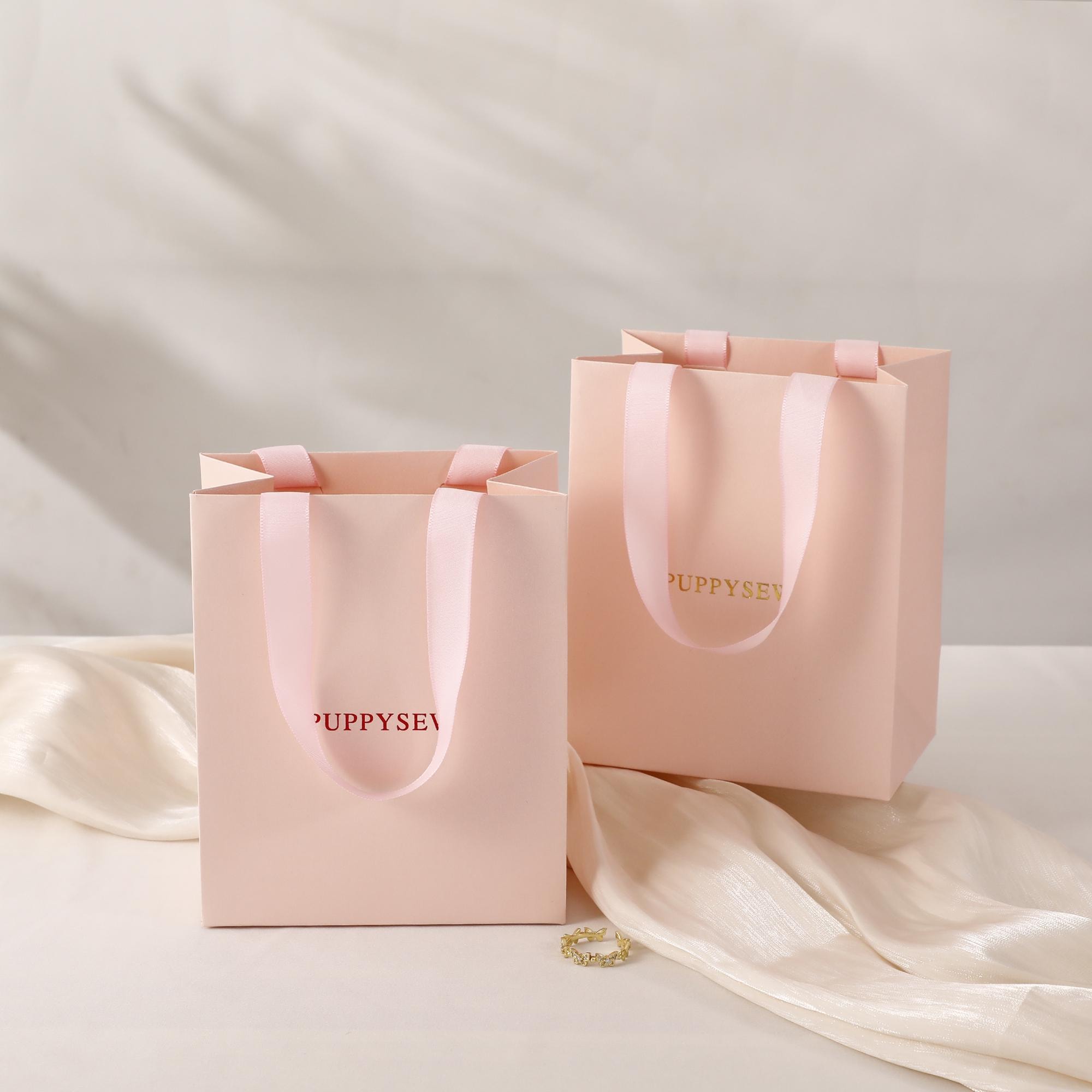 Pearlescent pink paper bags with custom logo printing in gold, demonstrating brand personalization for jewelry businesses