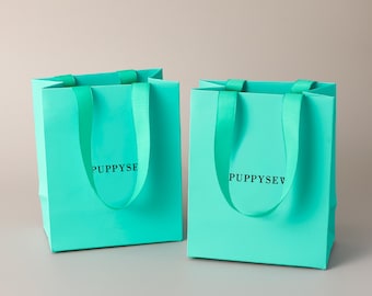 Bolsas de regalo de papel color turquesa con logotipo personalizado y asas de satén, ideales para recuerdos de boda o para empaques de boutique.