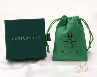 May include: A green velvet jewellery pouch with a black and white illustration of a dog in a box. The pouch has the text "PUPPYSEW" printed on it. The pouch is sitting on a white surface next to a green box with the text "CENTURYHOT" printed on it.