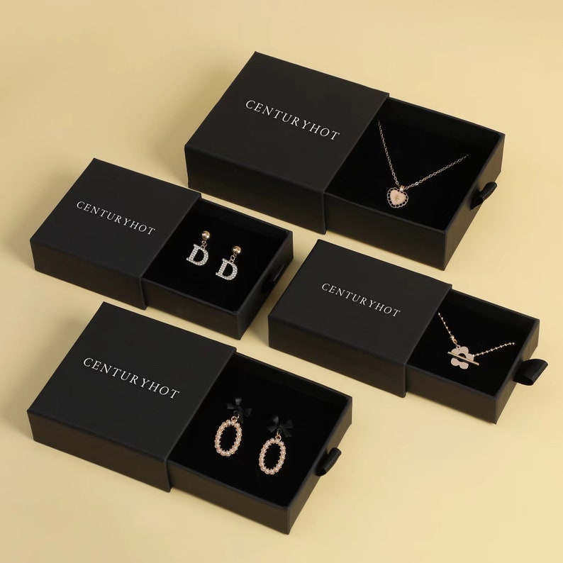 May include: Four black gift boxes with sliding drawers, each containing a piece of jewelry. The boxes are labeled "Centuryhot" and feature a variety of necklaces and earrings.