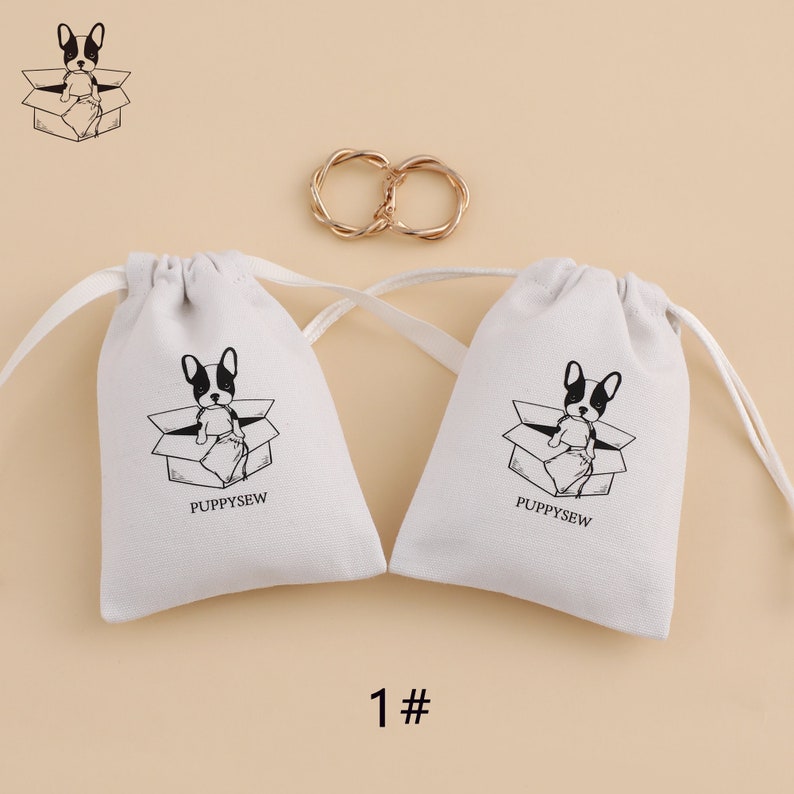 May include: Two white cotton drawstring bags with black and white illustrations of a dog sitting in a box. The text "PUPPYSEW" is printed on each bag.