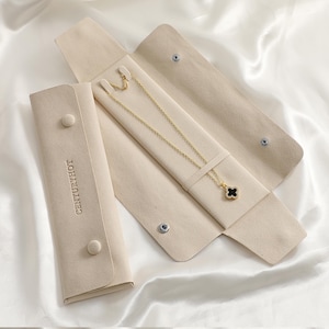 May include: A gold-tone chain necklace with a black four-leaf clover pendant featuring a border of small clear stones. The necklace is displayed inside an open, beige, soft-touch jewellery roll with the text CENTURYHOT embossed on the flap.