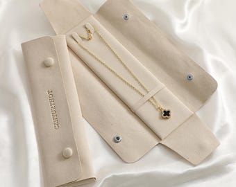 May include: A gold-tone chain necklace with a black four-leaf clover pendant featuring a border of small clear stones. The necklace is displayed inside an open, beige, soft-touch jewelry roll with the text CENTURYHOT embossed on the flap.