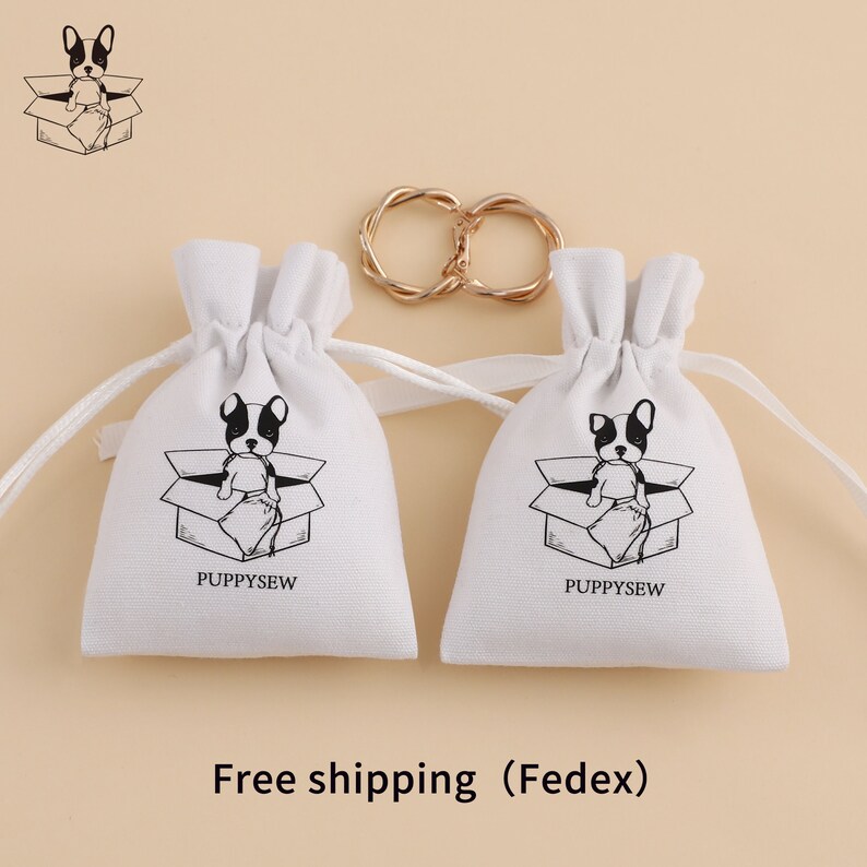 May include: Two white drawstring bags with a black and white illustration of a French bulldog sitting in a box. The bags have the text "Puppysew" printed on them.