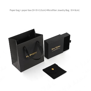 May include: Black paper gift bag with gold lettering that says "PU PYSEW".  The bag is next to a black gift box with a sliding lid that says "Best Wishes" in gold lettering.  There is also a small black velvet jewellery bag with a gold button.
