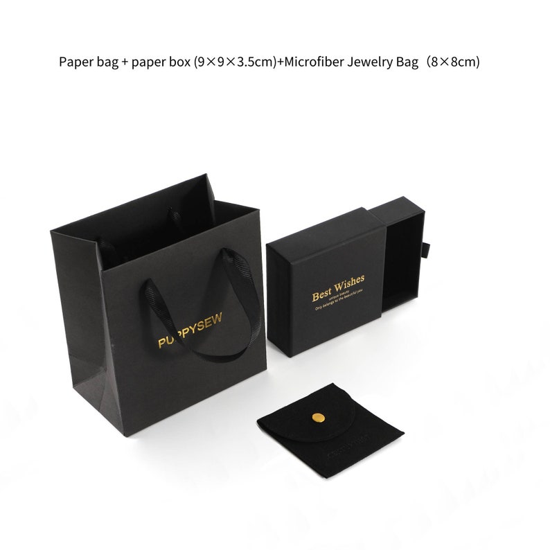 May include: Black paper gift bag with gold lettering that says "PU PYSEW".  The bag is next to a black gift box with a sliding lid that says "Best Wishes" in gold lettering.  There is also a small black velvet jewellery bag with a gold button.