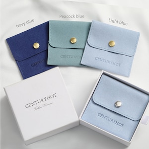 May include: Four small, square, fabric pouches in navy blue, peacock blue, light blue, and light blue. Each pouch has a small, round, gold button closure and the text "CENTURYHOT" printed on the front. The pouches are sitting on a white surface.