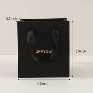 May include: Black paper gift bag with black ribbon handles and gold lettering that says "Puppysev". The bag measures 14 cm tall, 12.5 cm wide, and 7 cm deep.