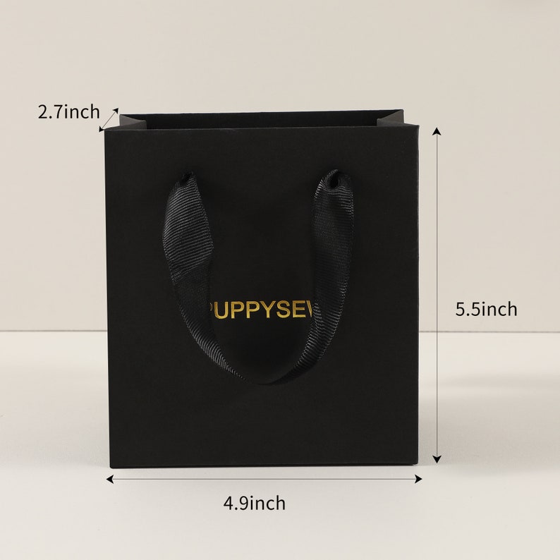 May include: Black paper gift bag with black ribbon handles and gold lettering that says "Puppysev". The bag measures 14 cm tall, 12.5 cm wide, and 7 cm deep.