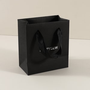 May include: Black paper shopping bag with black ribbon handles and the word "PYSEW" printed in silver foil.