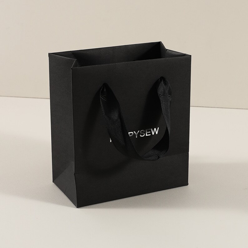 May include: Black paper shopping bag with black ribbon handles and the word "PYSEW" printed in silver foil.