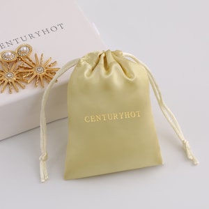 May include: A light yellow satin drawstring bag with the text "CENTURYHOT" printed in gold on the front.