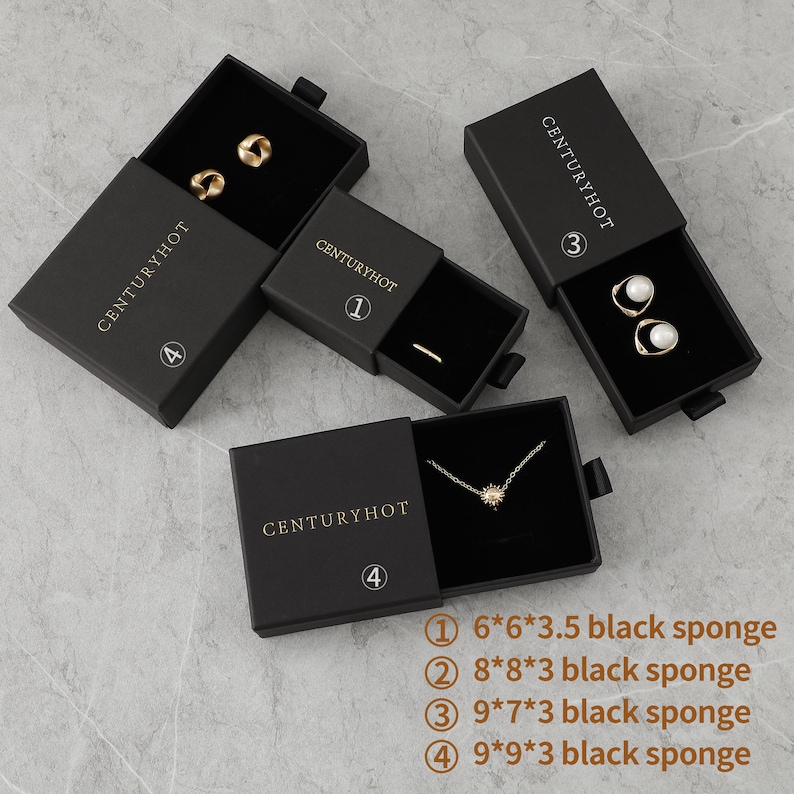 May include: Four black boxes with gold lettering that says "CENTURYHOT" and a number from 1 to 4. Each box contains a different piece of jewelry: a pair of gold earrings, a gold ring, a pair of pearl earrings, and a gold necklace with a star pendant. The boxes are on a gray textured surface. The text below the boxes reads: "① 6*6*3.5 black sponge ② 8*8*3 black sponge ③ 9*7*3 black sponge ④ 9*9*3 black sponge"