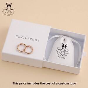 May include: A white box with the text "CENTURYHOT" printed on the top. The box contains a pair of gold-colored twisted hoop earrings. The box is open and a white drawstring bag with the text "PUPPYSEW" and a black and white illustration of a dog in a box is visible inside.