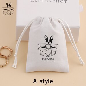May include: White cotton drawstring bag with a black and white illustration of a French bulldog sitting in a box. The text "PUPPYSEW" is printed below the illustration. The bag is on a light brown surface.