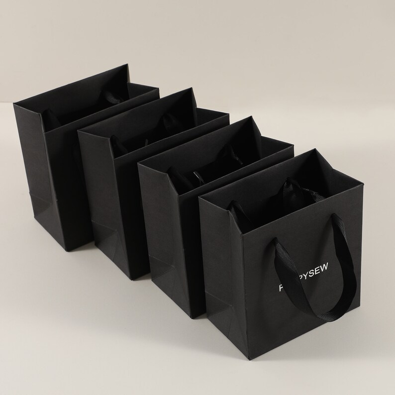 May include: Four black paper gift bags with black ribbon handles. The bag on the right has the text "FORSYTHEW" printed on the front.