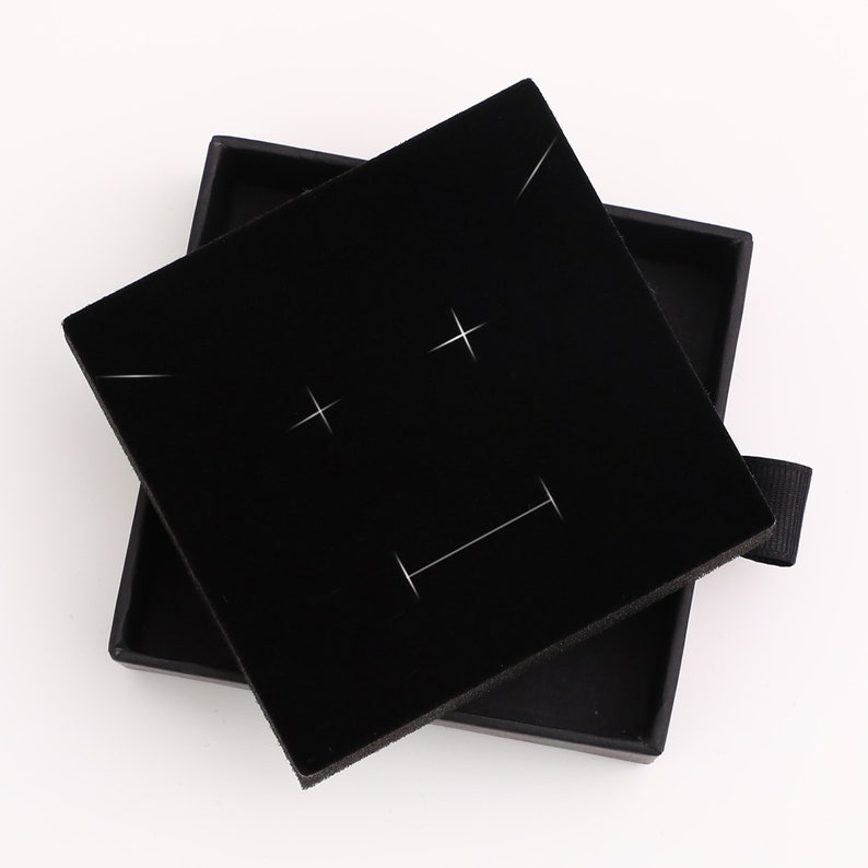 May include: Black velvet jewelry box with a square lid. The lid has a white design of two plus signs and a horizontal line.