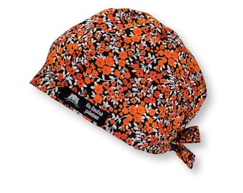 May include: A black scrub cap with a floral pattern in orange and white. The cap has a tie at the back and a small label that says "la loutre piqueuse".
