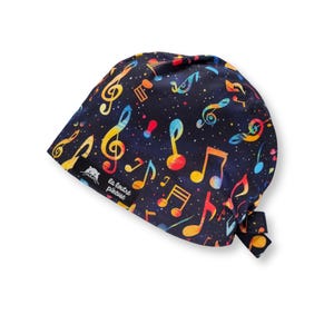 Può includere: Un cappello chirurgico blu scuro con un motivo colorato di note musicali. Le note sono in tonalità di giallo, arancione, rosso e blu. Il cappello ha una chiusura con lacci e una piccola etichetta bianca con testo.