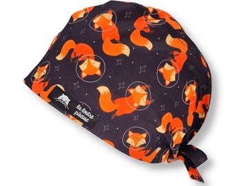 May include: Black scrub cap with a repeating pattern of orange foxes in space suits on a dark blue background. The text "la loutre piqueuse" is printed on the cap.