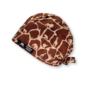 Peut inclure: Un bonnet de chirurgien marron et beige avec un imprimé girafe. Le bonnet présente un motif répété de taches de girafe et de silhouettes d'animaux. Une petite étiquette noire avec du texte blanc est cousue sur le côté. Le bonnet est noué à l'arrière.
