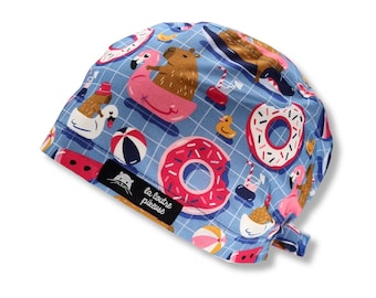 May include: A blue and white patterned scrub hat with a capira, flamingo, donut, and watermelon design. The hat has a black label with the text "la loutre piqueuse".
