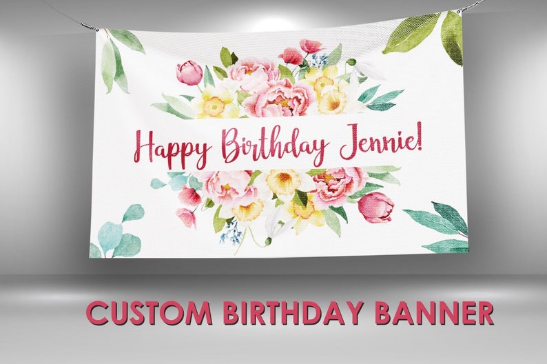 May include: A white banner with a floral design in shades of pink, yellow, and green. The banner says "Happy Birthday Jennie!" in red lettering.  Custom Birthday Banner.