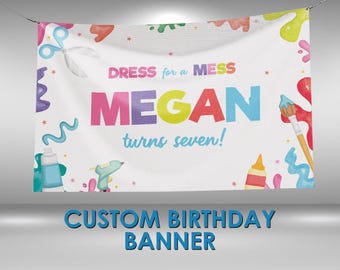 May include: White banner with the text "DRESS for a MESS" and "MEGAN turns seven!" in colorful letters. The banner is decorated with paint splatters, scissors, paintbrushes, and other art supplies. The words "CUSTOM BIRTHDAY BANNER" are at the bottom.