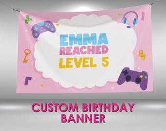 May include: Pink custom birthday banner with the text "EMMA REACHED LEVEL 5" in blue, pink, and yellow. The banner features game controller and headset graphics. The words "CUSTOM BIRTHDAY BANNER" are at the bottom.