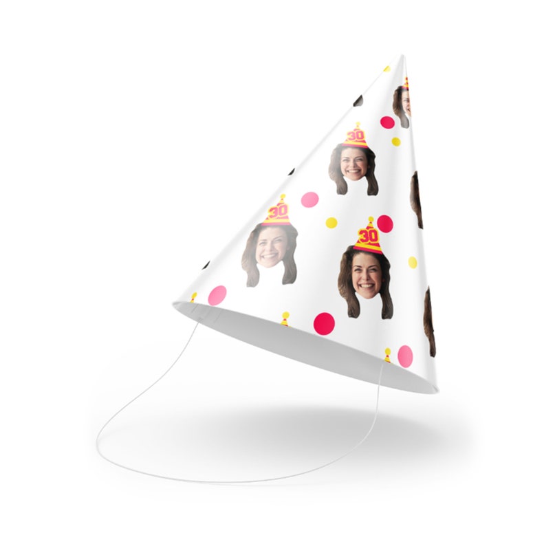 May include: White party hat decorated with repeating images of a smiling person wearing a party hat with the number 30. The hat also features pink and yellow polka dots and a white string.
