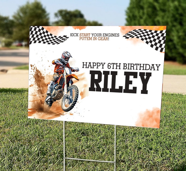 May include: A white and orange birthday sign with a checkered flag design. The sign features a photo of a dirt bike rider and the text "Kick start your engines put'em in gear! Happy 6th Birthday Riley".