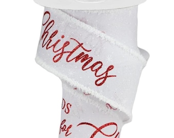 May include: A white fabric ribbon on a spool featuring a subtle snowflake pattern and the red glittery text "ALL ROADS lead home for Christmas" printed in a mix of block and cursive fonts with frayed edges along the sides of the ribbon.