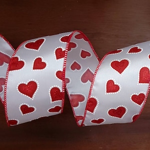 May include: White satin ribbon with a red heart pattern. The hearts have a white outline and a glittery texture.