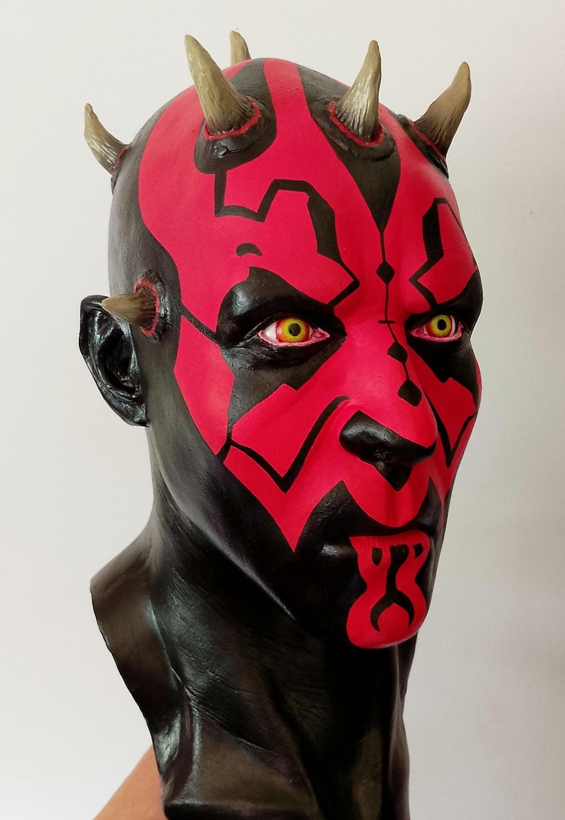 May include: A red and black painted bust of Darth Maul from Star Wars. The bust has horns and yellow eyes.