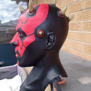 May include: A black and red Darth Maul mask with yellow horns. The mask is made of a hard plastic and has a detailed paint job.