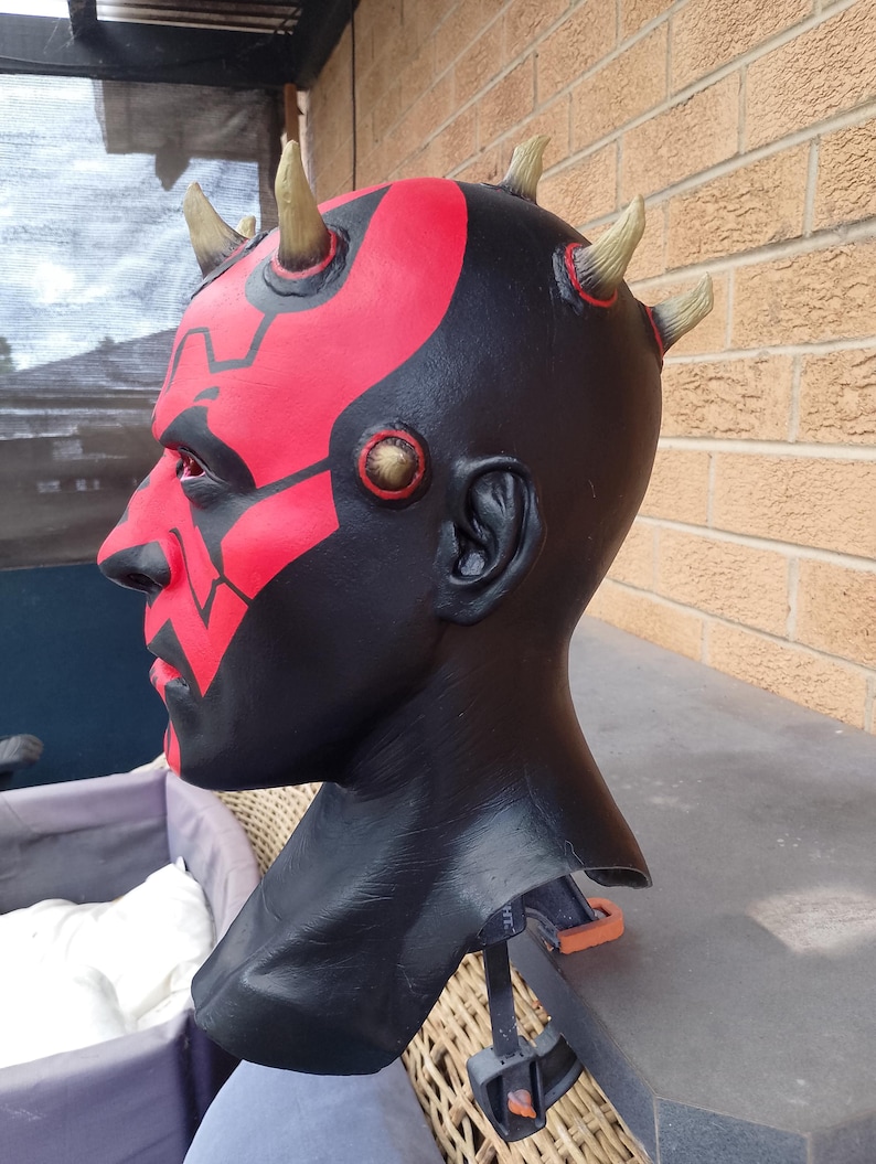 May include: A black and red Darth Maul mask with yellow horns. The mask is made of a hard plastic and has a detailed paint job.