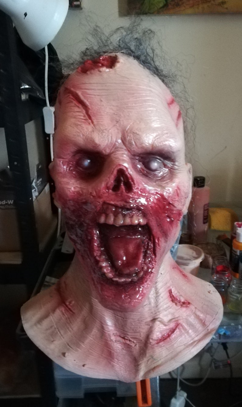 May include: A realistic zombie mask with a pale, bloody face, open mouth, and visible teeth. The mask has a red, bloody, and gory appearance.
