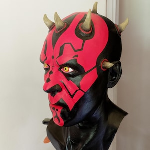 May include: A red and black Darth Maul bust with horns. The bust is made of a smooth, painted material and has a detailed face.