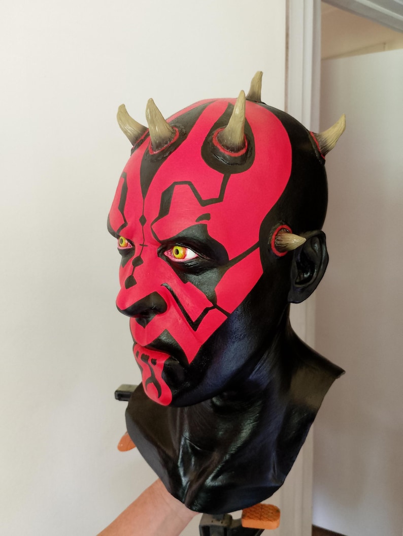 May include: A red and black Darth Maul bust with horns. The bust is made of a smooth, painted material and has a detailed face.