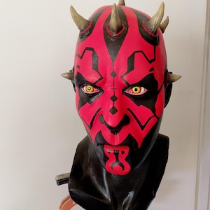 May include: A red and black Darth Maul bust with yellow eyes and horns. The bust is made of plastic and is a replica of the character from the Star Wars franchise.
