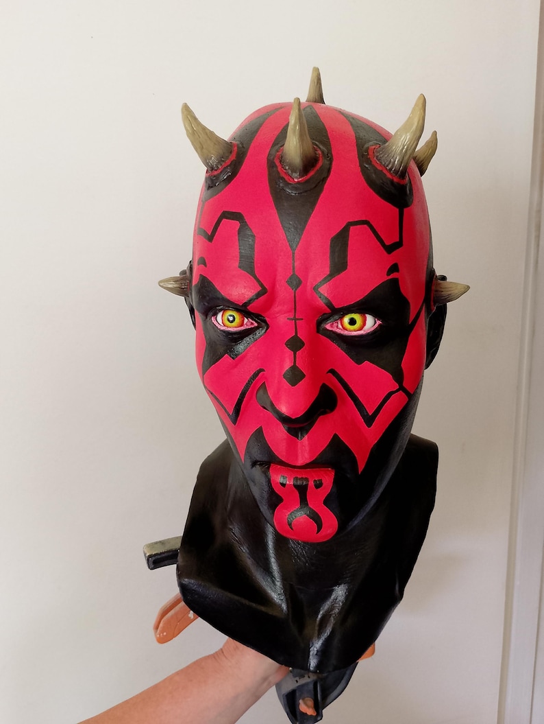 May include: A red and black Darth Maul bust with yellow eyes and horns. The bust is made of plastic and is a replica of the character from the Star Wars franchise.